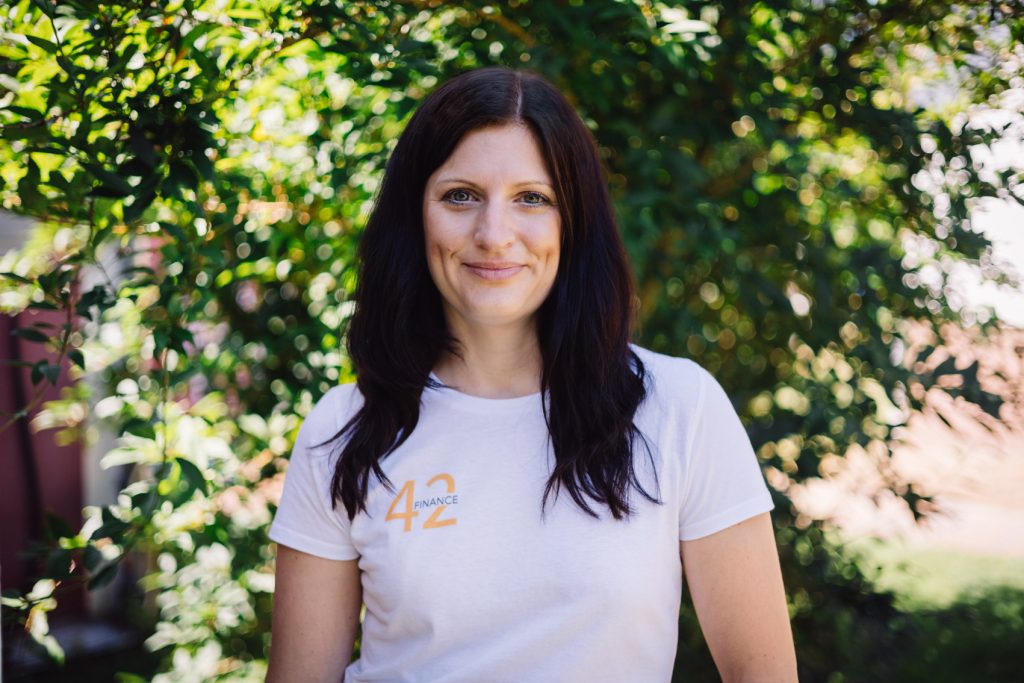 Sabrina lächelt in die Kamera, sie hat lange dunkle Haare und trägt ein weißes T-Shirt mit dem Logo von 42Finance.